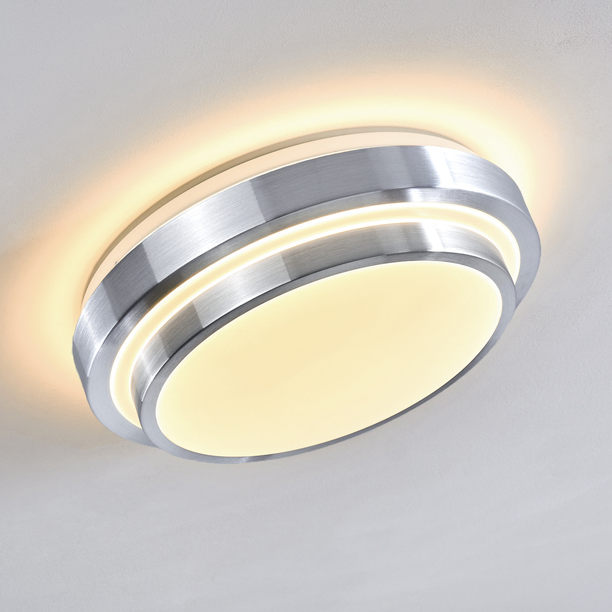 Eine moderne Deckenleuchte. Sie hat eine gebürstete Metalloberfläche mit kreisförmigem Design und strahlt warmes, diffuses Licht aus.