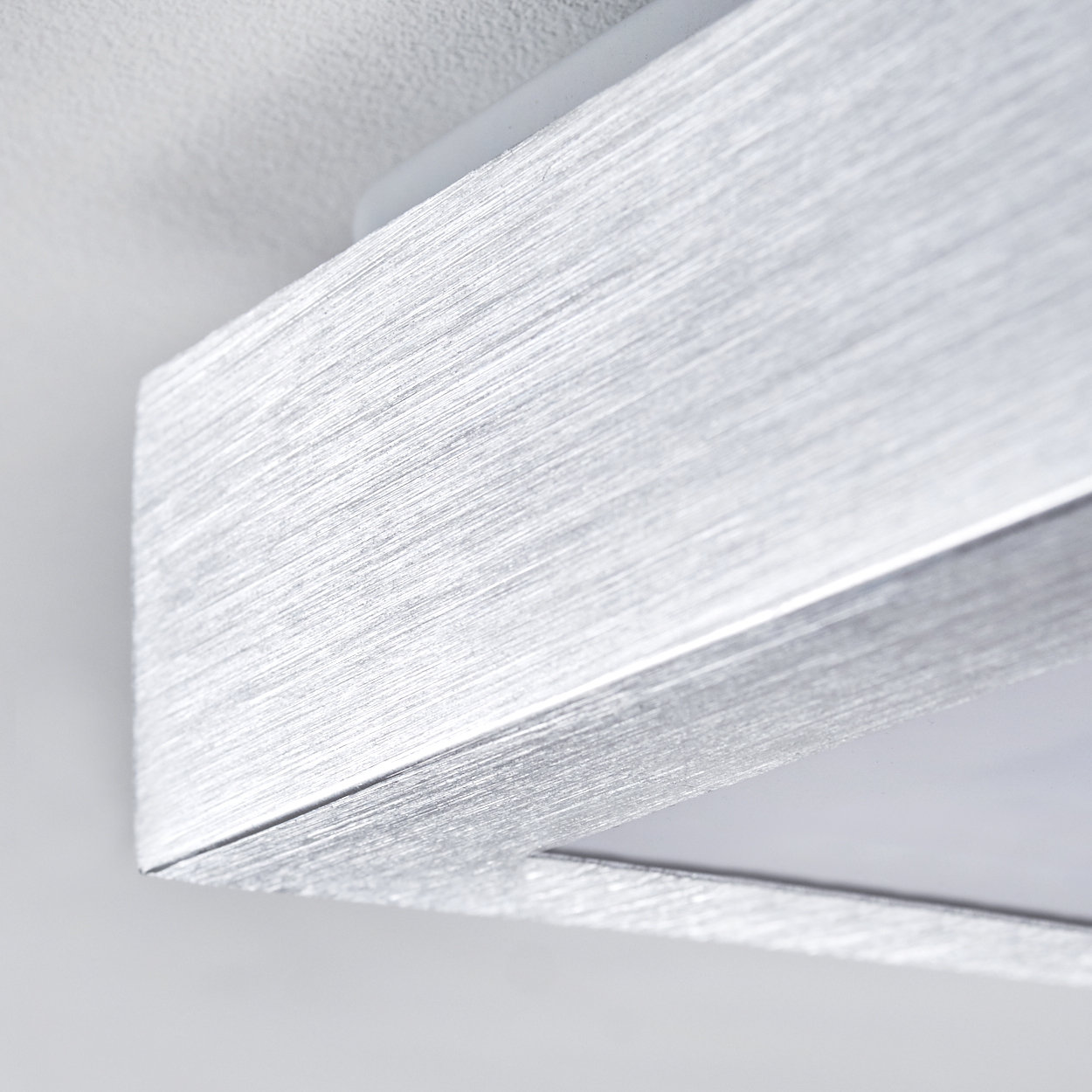 Nahaufnahme einer silbernen, strukturierten Leuchte. Die gebürstete Metalloberfläche reflektiert das Licht. Sie ist an einer weißen Decke befestigt.