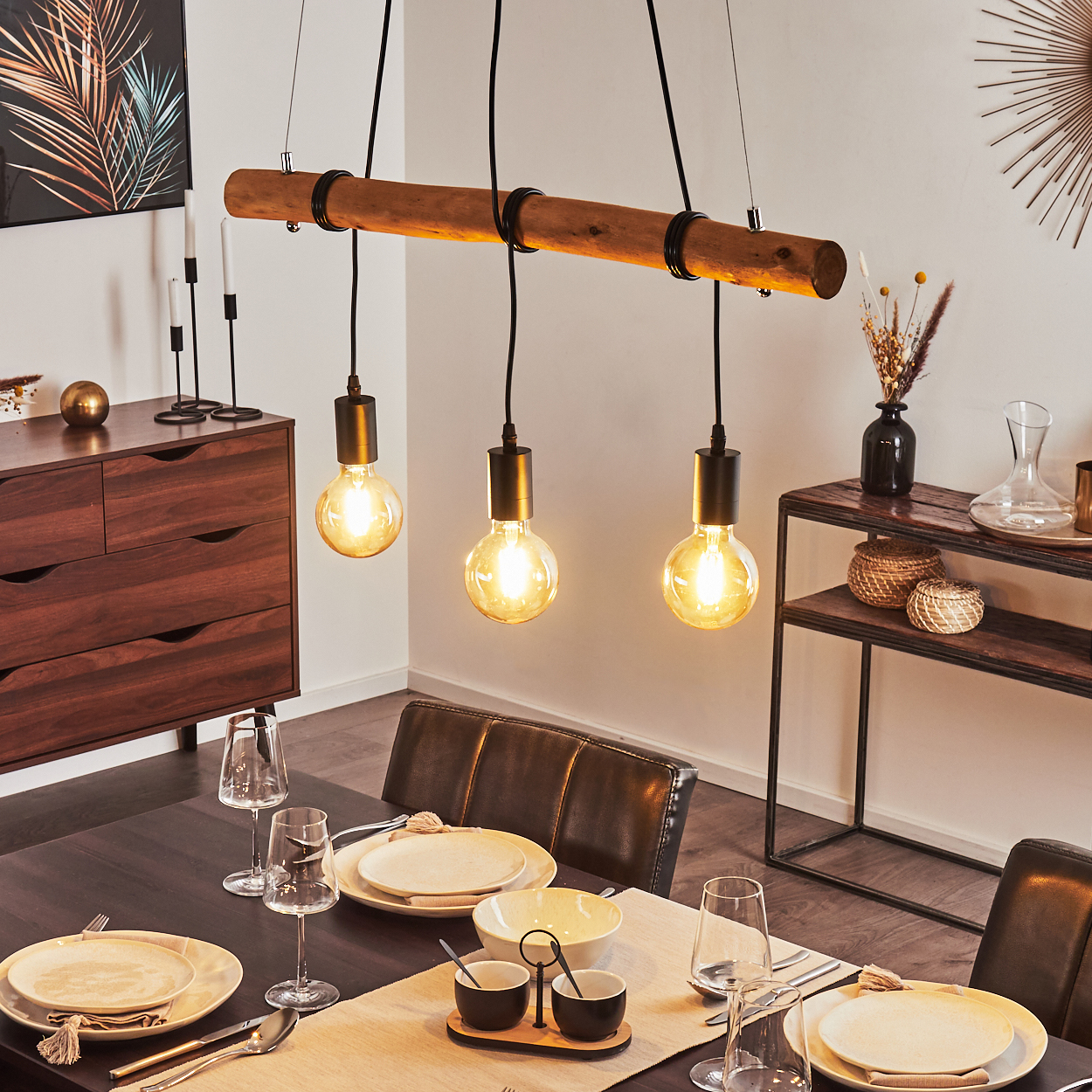 Esszimmer mit Holzbalken-Leuchte, gedecktem Tisch, Sideboard und Beistelltisch mit Dekoration.