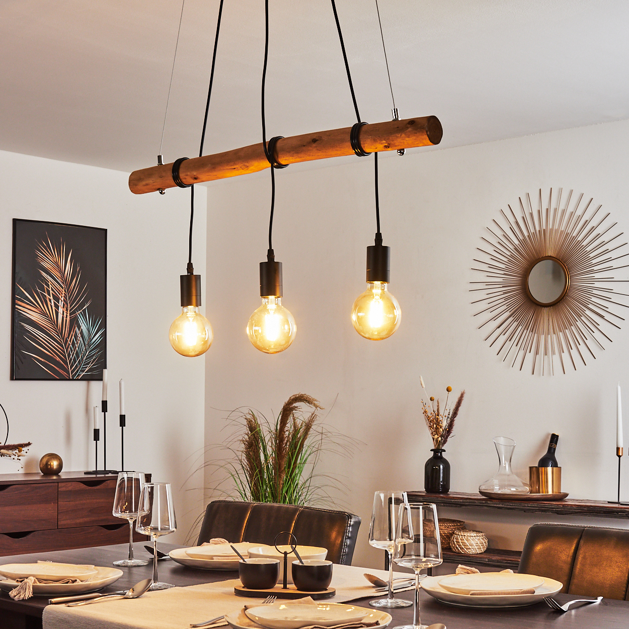 Esszimmer mit Tischdeko, drei Hängeleuchten und Dekoration. Ein Spiegel und Kunstwerk an der Wand.
