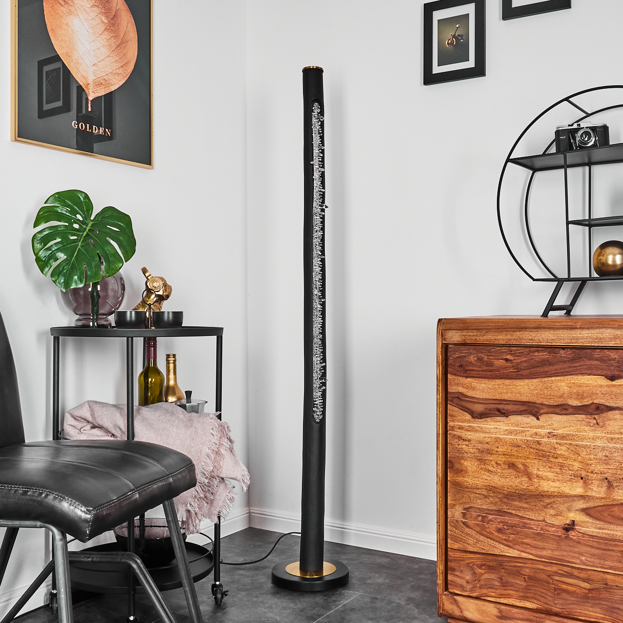 Ein Raum mit einer schwarzen Stehlampe, einem Holzschrank, einem schwarzen Stuhl und einem runden schwarzen Tisch mit Dekorationen.