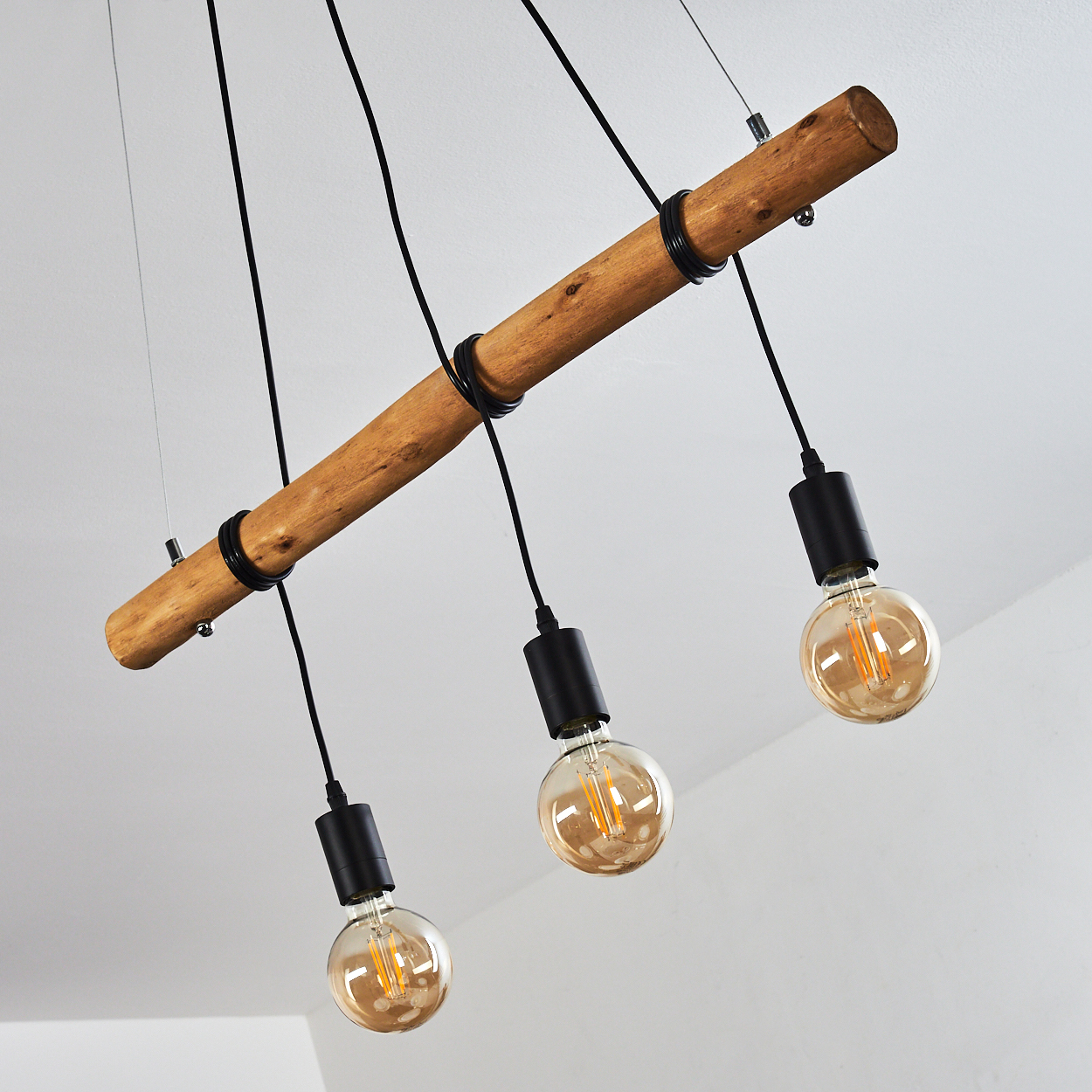 Ein Holzbalken mit drei Hängelampen. Jede hat einen schwarzen Sockel und eine runde, leuchtende Glühbirne. Die Decke ist weiß.