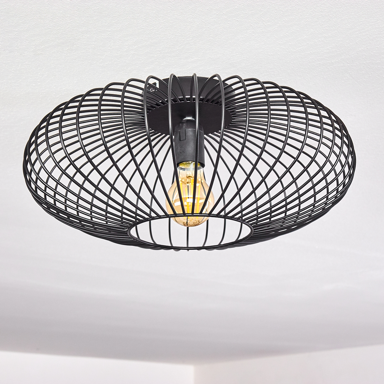 Eine schwarze Deckenleuchte aus Metall. Sie hat ein käfigartiges Design um eine Glühbirne. Der Hintergrund ist eine weiße Decke.