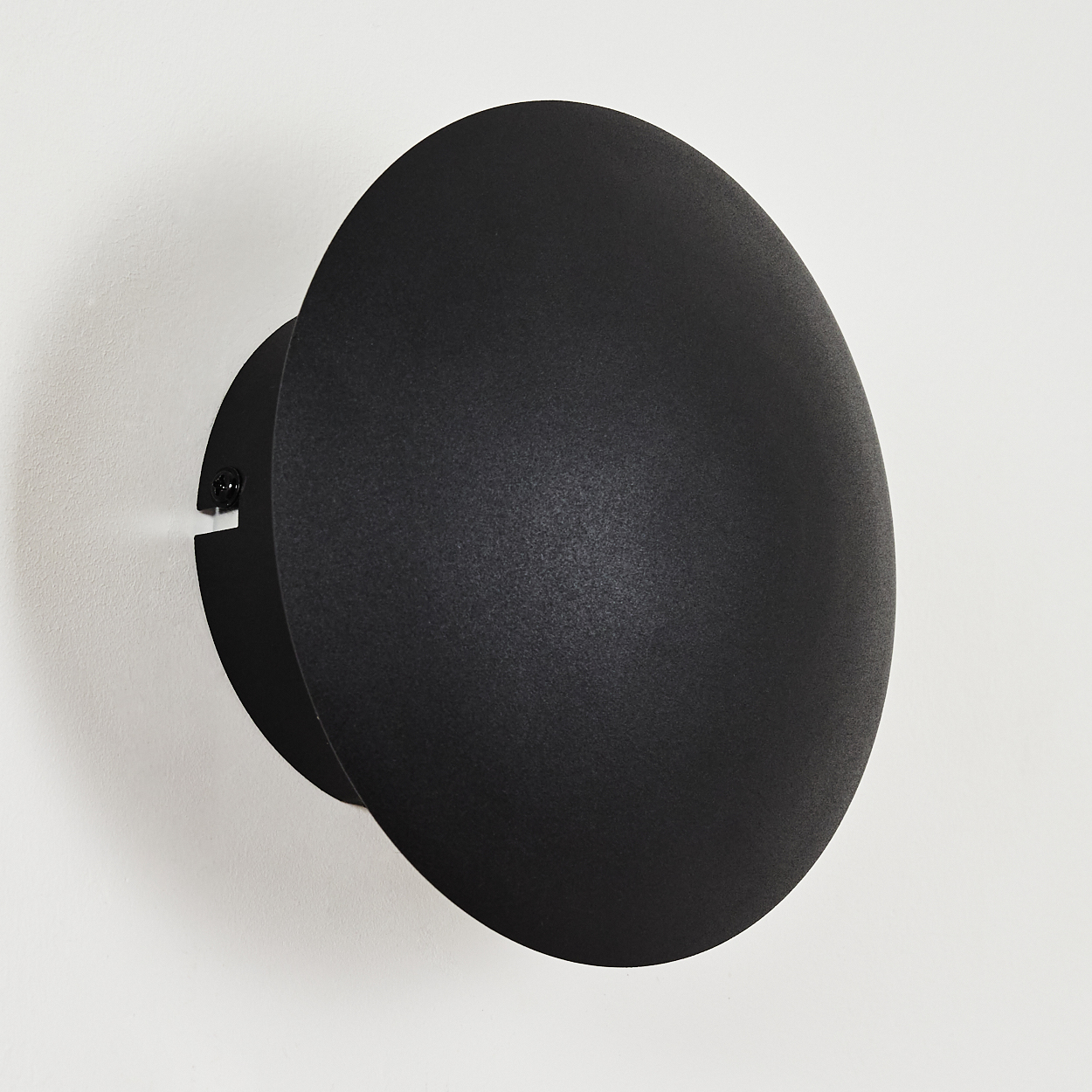 Eine schwarze, runde Wandleuchte ist an einer weißen Wand montiert. Die Lampe hat einen kreisförmigen Schirm und eine Montagebasis.