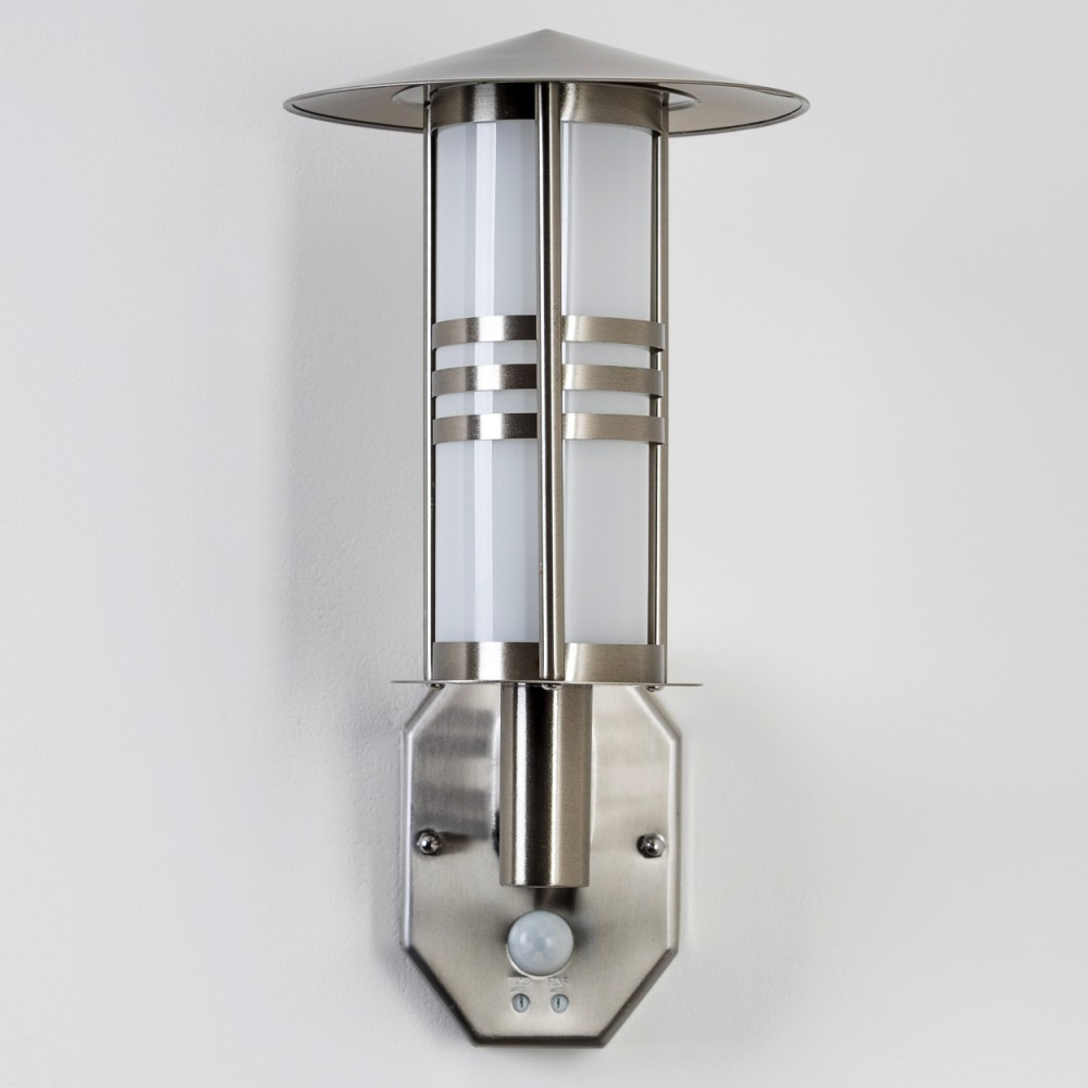 Eine silberne Außenlampe ist an einer weißen Wand angebracht. Sie hat einen Bewegungssensor und ein zylindrisches Design mit einem oberen Schirm.