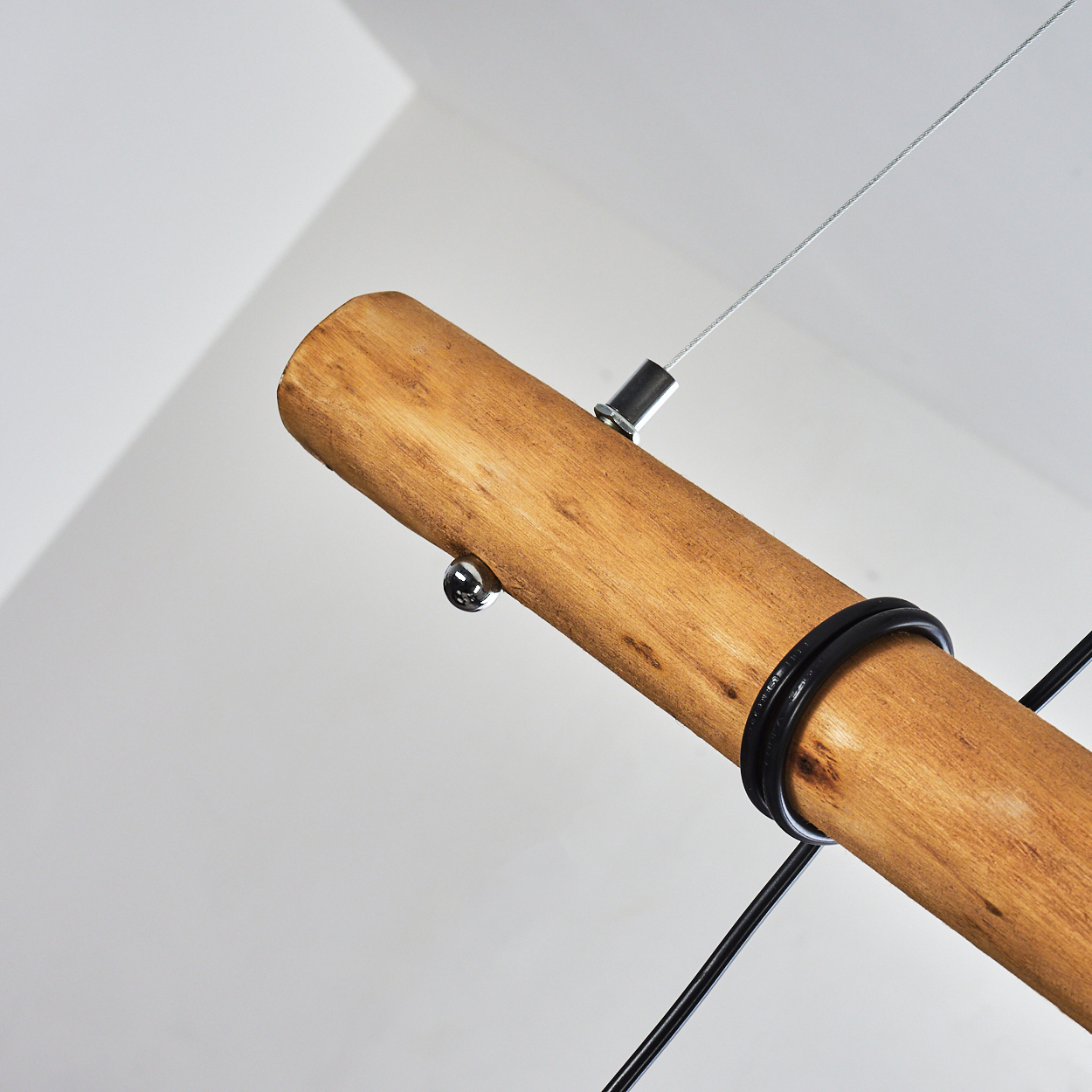 Nahaufnahme einer Leuchte. Ein Holzbalken wird von einem Metallkabel gehalten. Schwarzer Draht wickelt sich um den Balken.