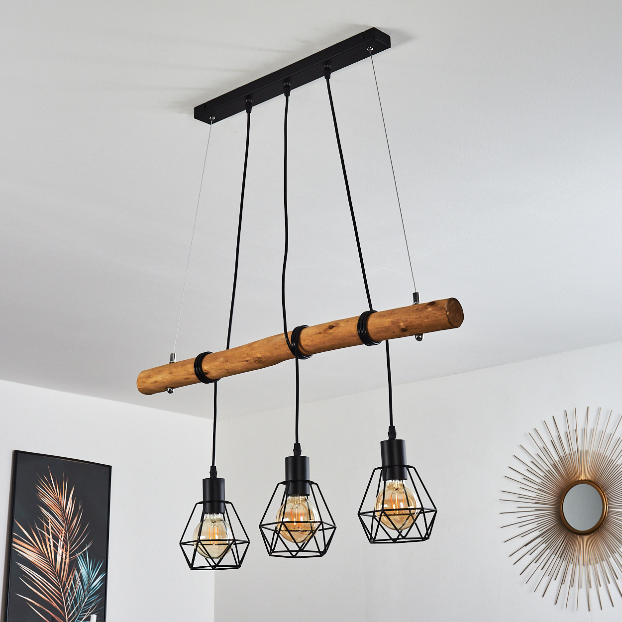 Ein Holzbalken mit drei Hängelampen. Jede Lampe hat einen schwarzen, käfigartigen Schirm und eine warme, leuchtende Glühbirne. Weißer Wandhintergrund.