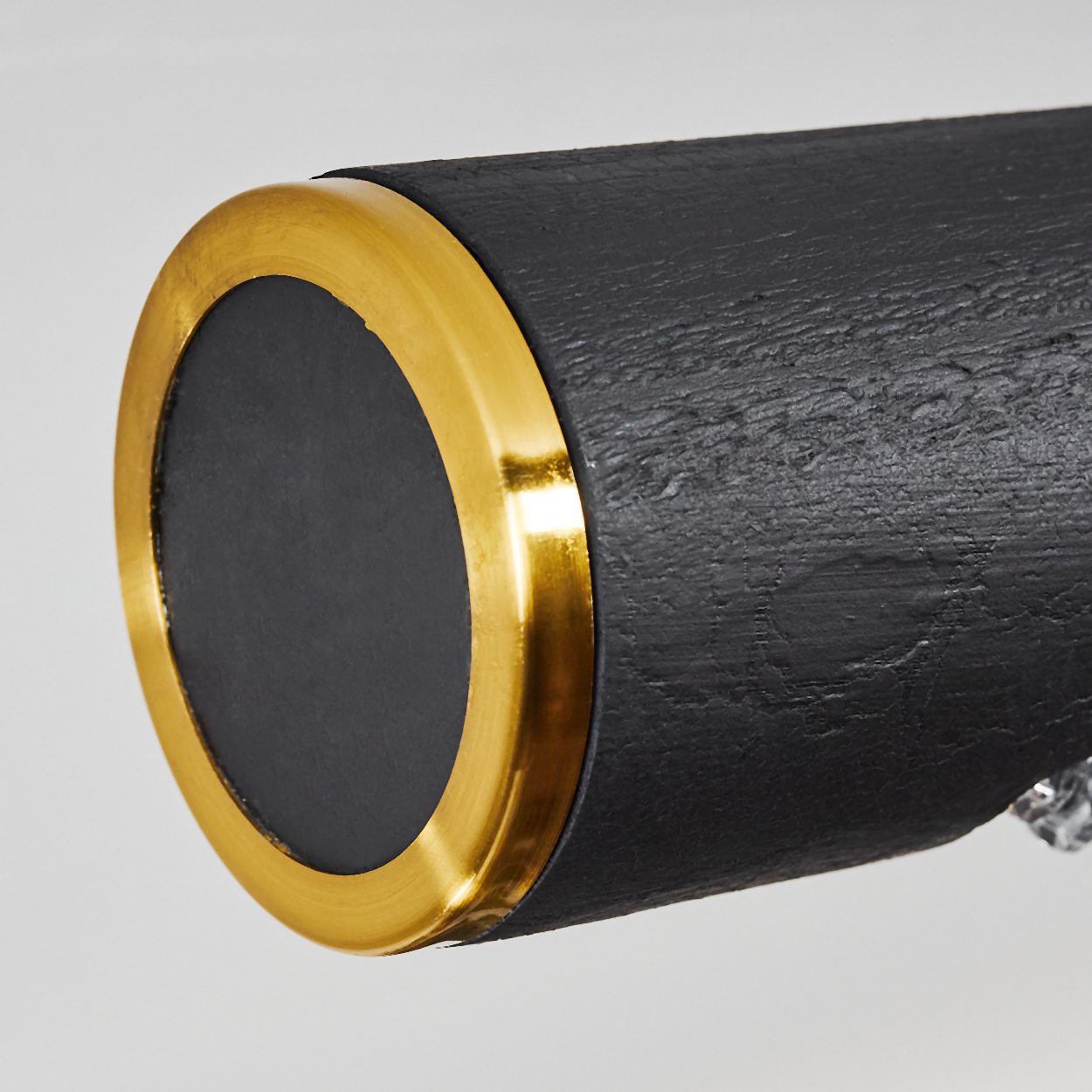 Nahaufnahme eines schwarzen Zylinders mit einem goldenen Ring am Ende. Die Oberfläche ist strukturiert. Der Hintergrund ist weiß.