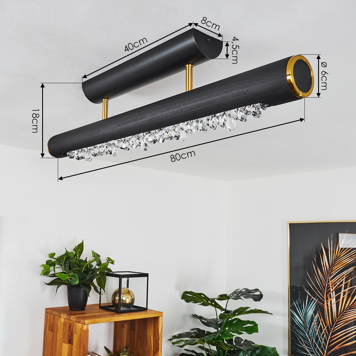 Eine schwarze Deckenlampe mit Kristallen und goldenen Akzenten. Auf dem Regal stehen Pflanzen und ein dekoratives Objekt.