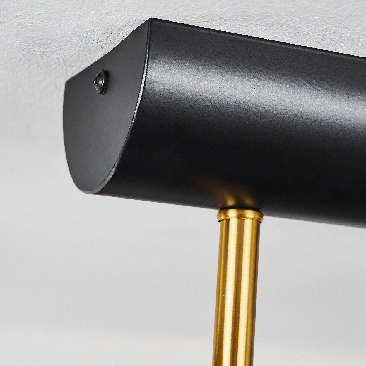 Nahaufnahme einer schwarzen Lampenhalterung mit goldener Stange und weißem Hintergrund. Die Lampe ist an der Decke montiert.