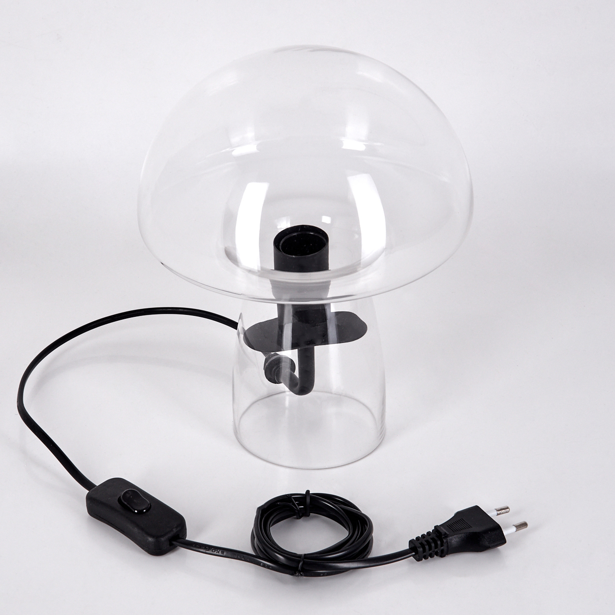 Eine klare pilzförmige Lampe mit schwarzem Sockel und Draht. Die Lampe steht auf einer weißen Oberfläche. Das Kabel hat einen Schalter und einen Stecker.