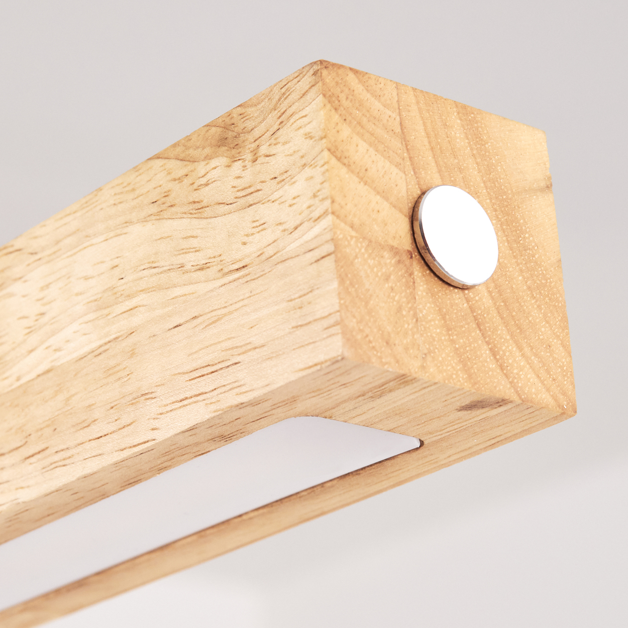 Nahaufnahme eines Holzblocks mit einer daran befestigten Metallscheibe. Das Holz ist hellbraun und hat sichtbare Maserung. Der Hintergrund ist weiß.