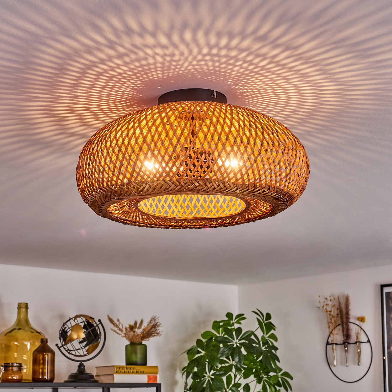 Eine Deckenleuchte aus geflochtenem Rattan wirft Schattenmuster. Darunter ein Regal mit Dekoration, Pflanzen und einem Globus.