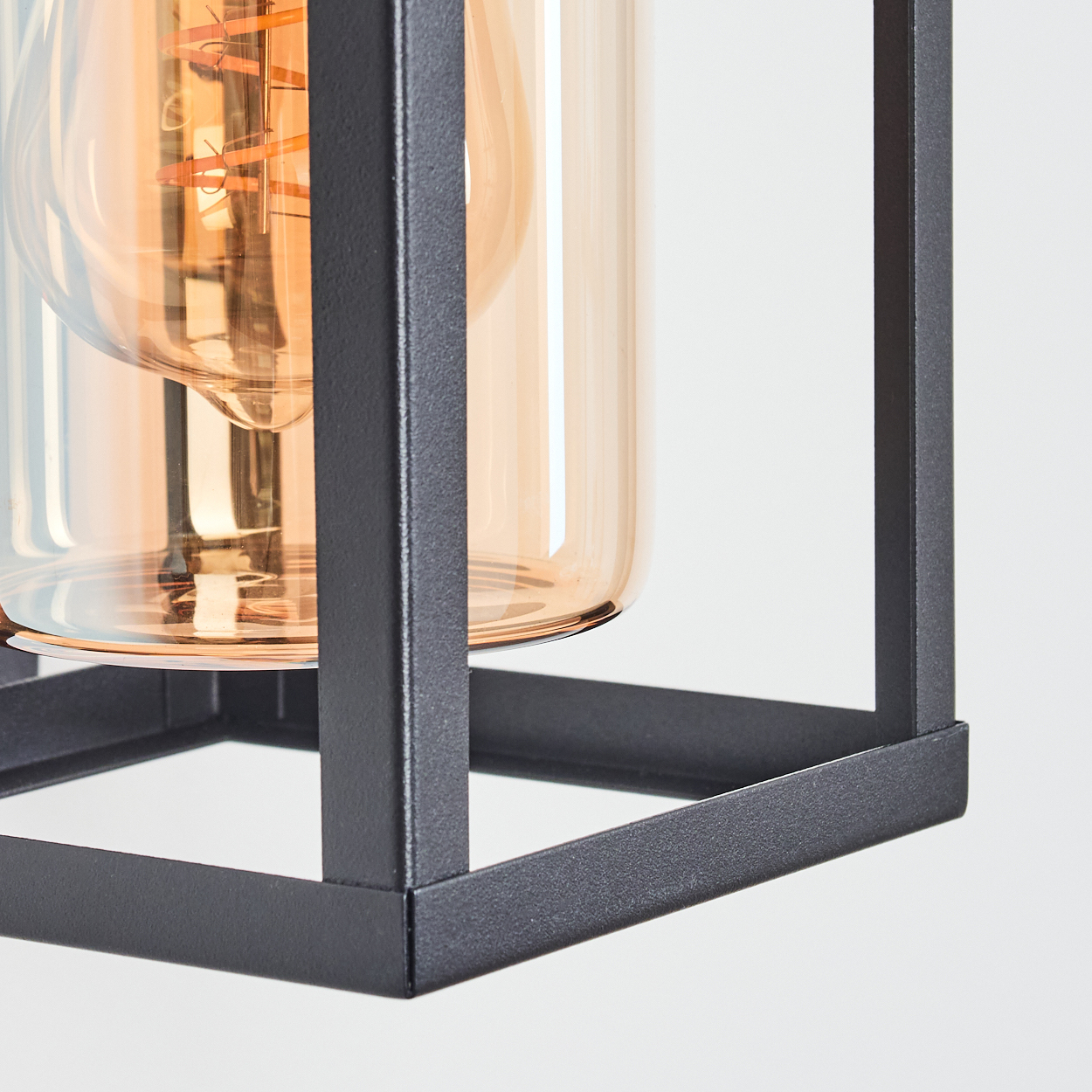 Nahaufnahme einer schwarzen Metallrahmen-Leuchte. Im Inneren befindet sich ein Glaskylinder mit einer warm getönten Glühbirne.