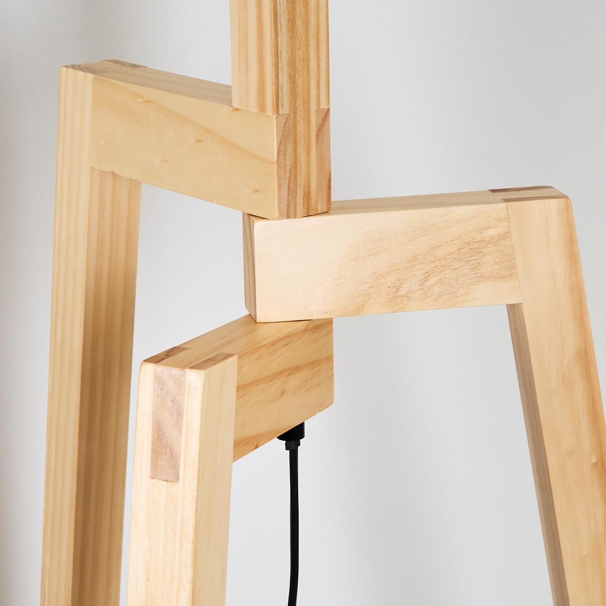 Nahaufnahme einer Holzlampenstruktur. Die Lampe besteht aus hellen Holzstücken, die miteinander verbunden sind. Ein schwarzes Kabel hängt herunter.