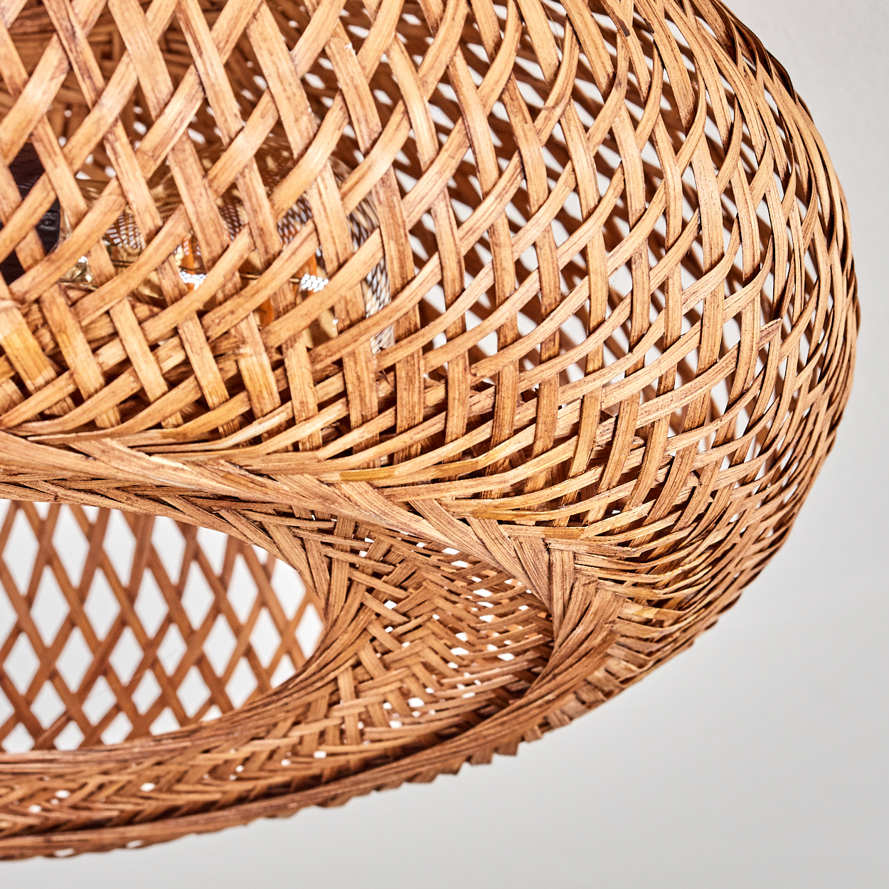 Nahaufnahme eines gewebten Lampenschirms aus Rattan. Der Schirm ist braun und hat eine runde Form mit einem Loch in der Mitte. Der Hintergrund ist weiß.