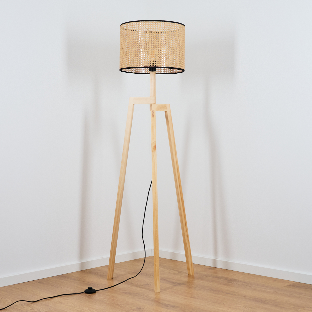 Eine Stehlampe aus Holz mit einem gewebten Lampenschirm steht in einer Ecke. Der Hintergrund sind weiße Wände und ein Holzboden.