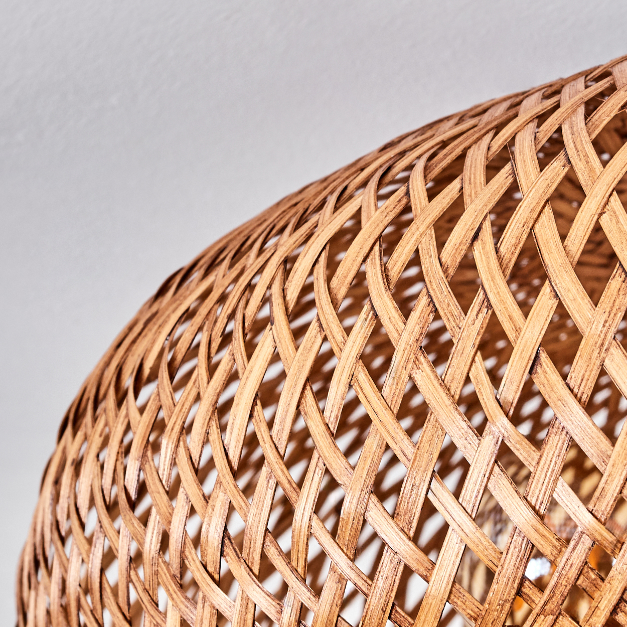 Nahaufnahme eines geflochtenen Lampenschirms aus Rattan. Das Geflecht ist detailliert, mit hellbrauner Farbe. Der Hintergrund ist eine schlichte weiße Oberfläche.