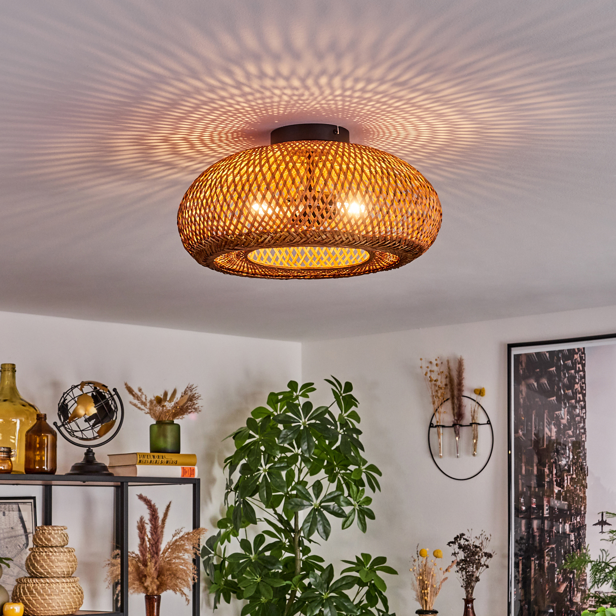 Eine gewebte Rattanlampe hängt von der Decke und wirft gemustertes Licht. Darunter ist ein Raum mit Pflanzen, Regalen und Kunstwerken dekoriert.