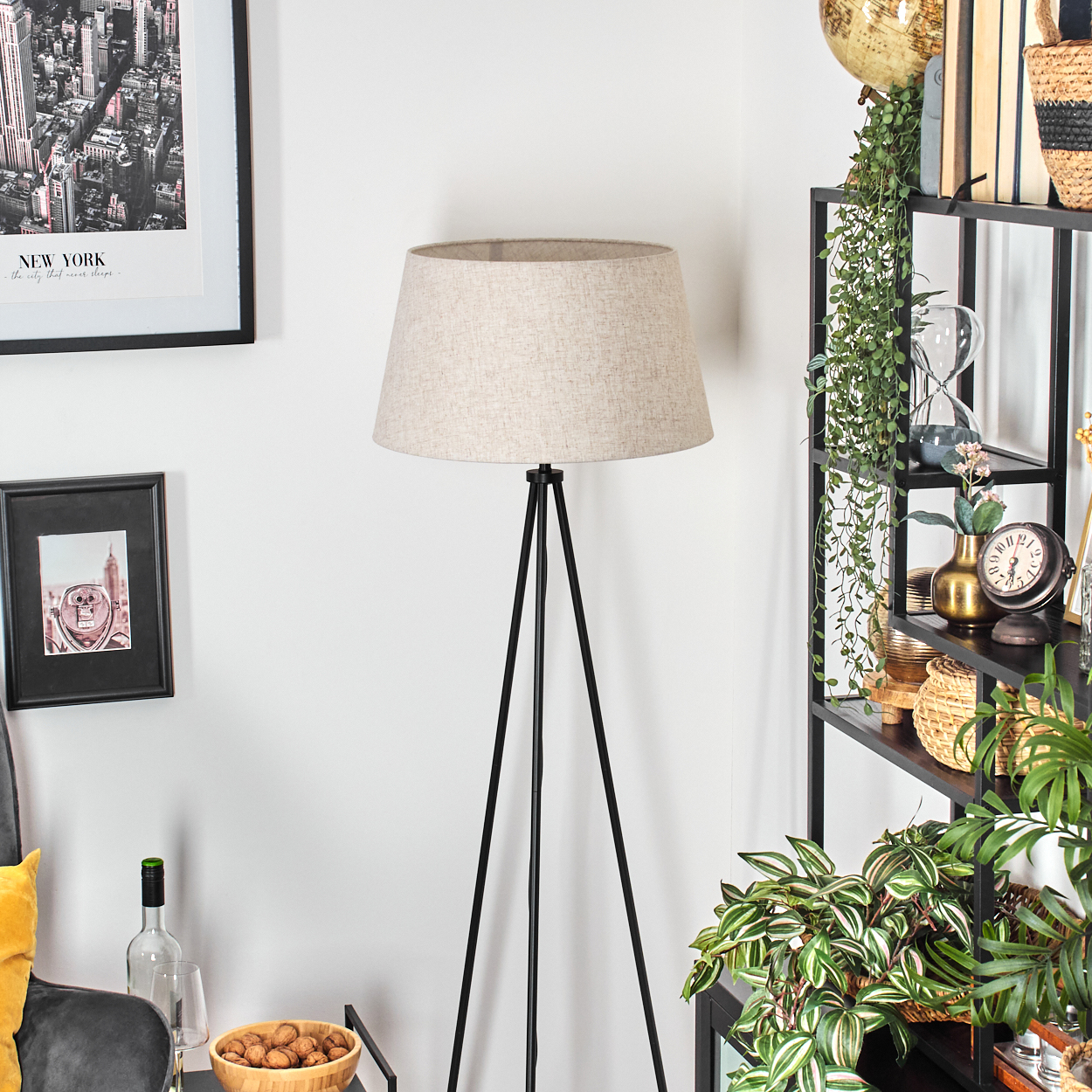 Ein Raum mit Lampe, Regalen mit Dekoration und einem Stadtposter. Eine Schüssel mit Nüssen und eine Weinflasche stehen auf einem kleinen Tisch.