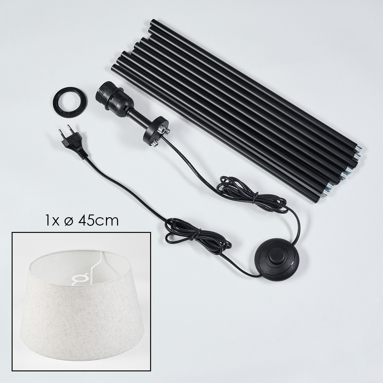 Lampenteile: schwarze Stangen, Fassung, Kabel, Fußschalter und Lampenschirm. Der Lampenschirm ist beige. Teile auf weißem Hintergrund.