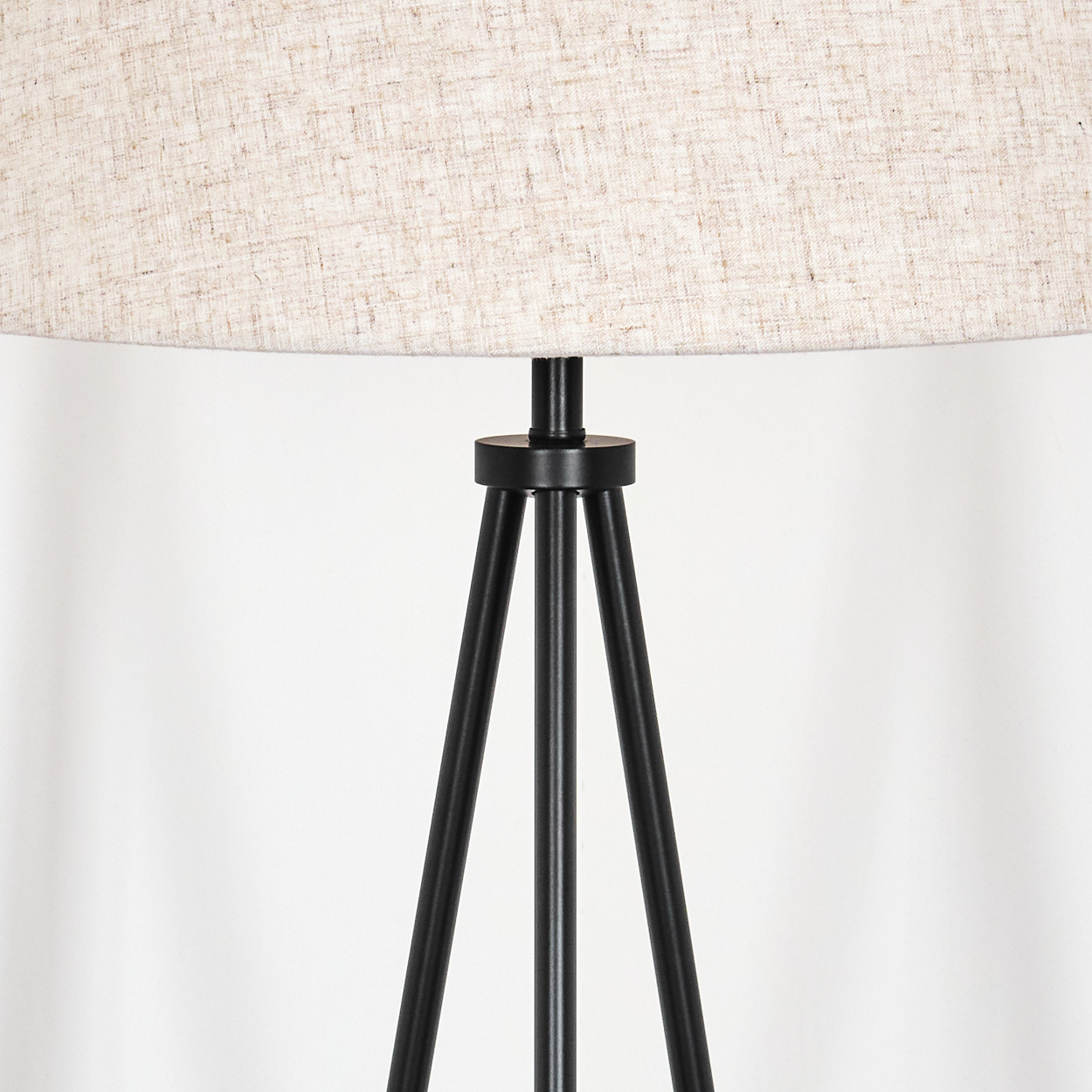 Eine schwarze Stehlampe mit Stativ und einem beigefarbenen Lampenschirm vor einer weißen Wand. Das Design ist schlicht und modern.