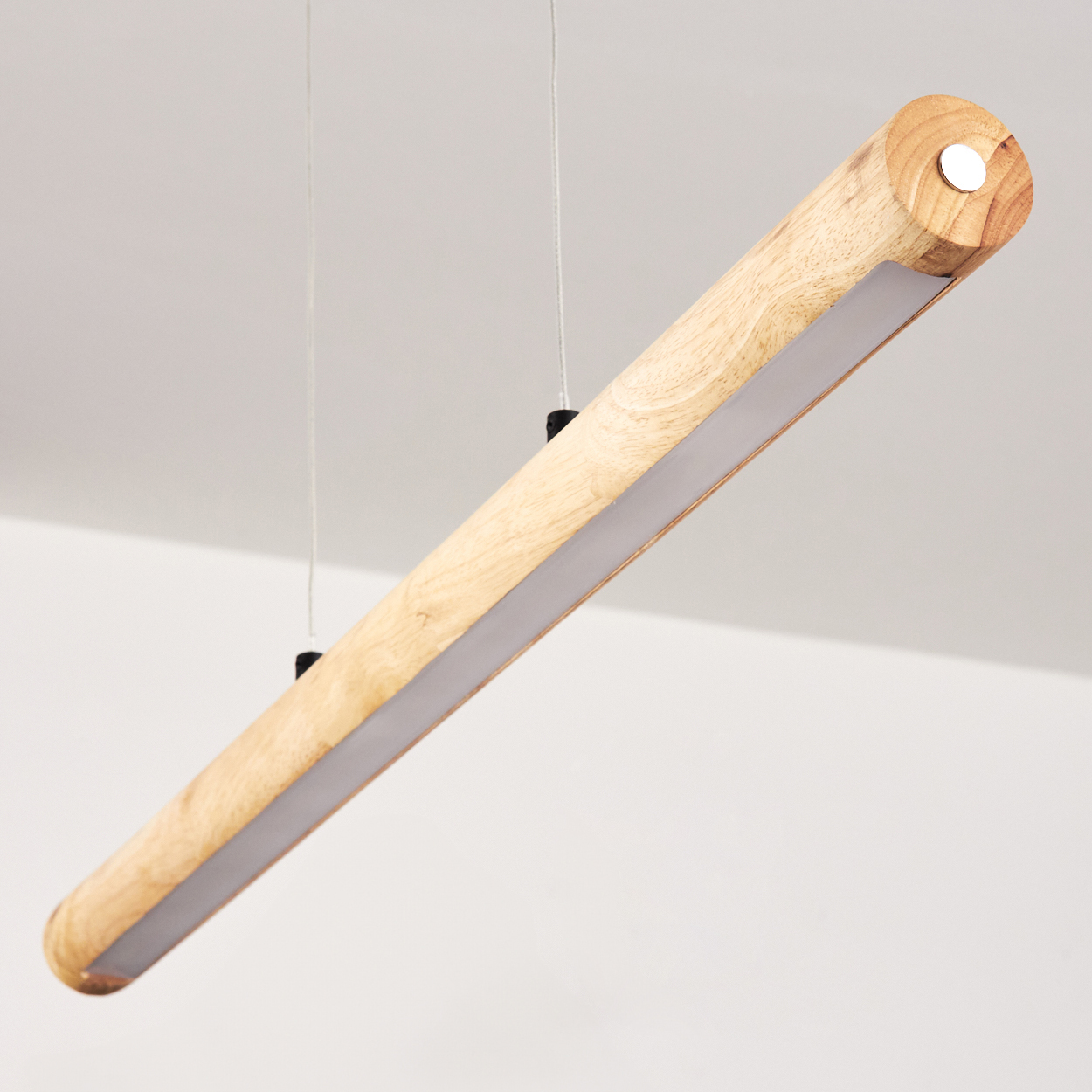 Eine zylindrische Holzleuchte hängt von der Decke. Sie hat einen Lichtstreifen an der Unterseite und ist mit dünnen Drähten befestigt.