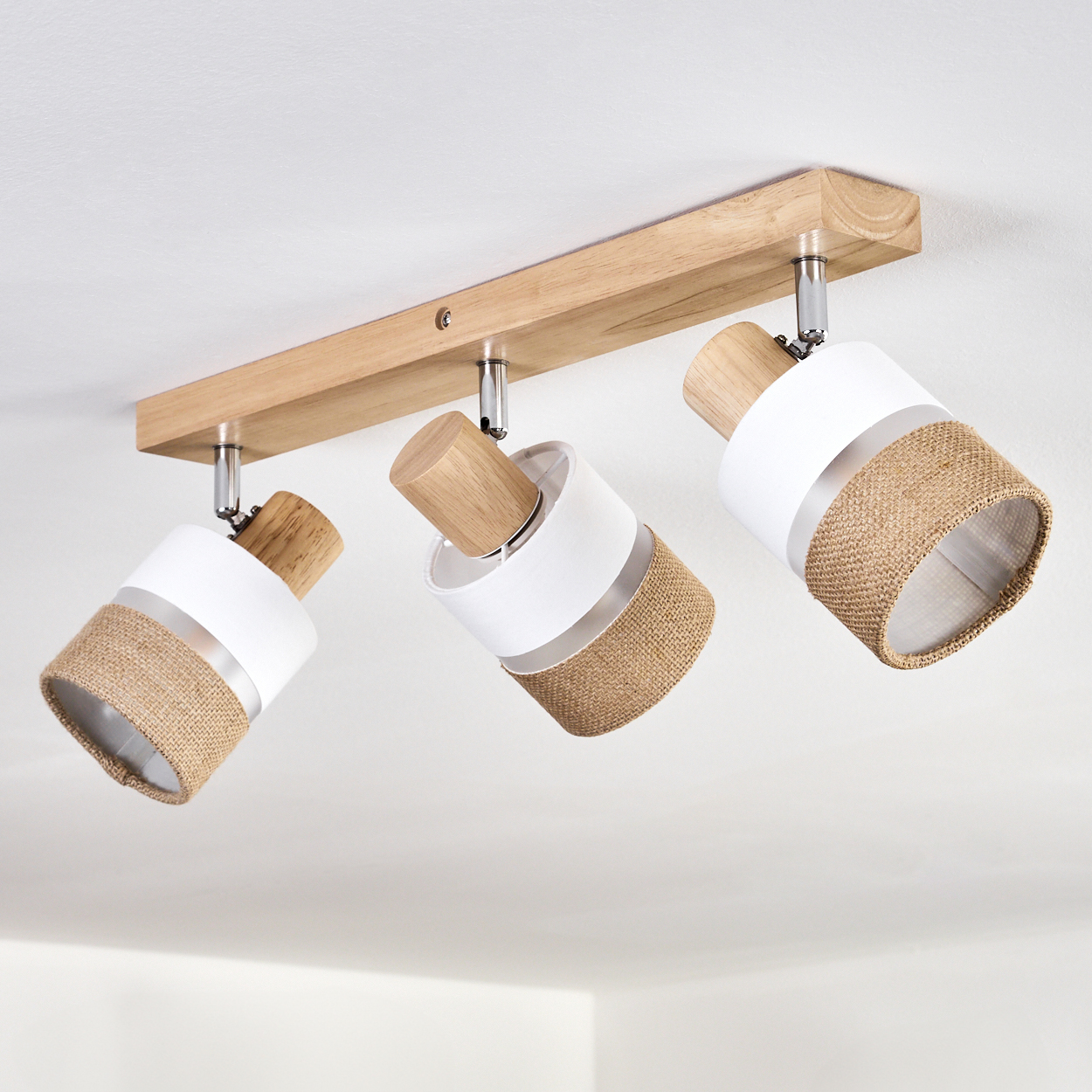 Eine Deckenleuchte mit drei Strahlern. Jeder Strahler hat einen weißen oberen Teil, einen mittleren Teil aus Jute und einen Holzsockel, montiert auf Holz.