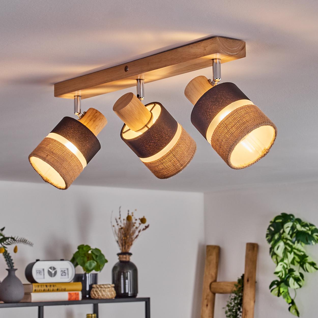 Eine Deckenleuchte mit drei verstellbaren Strahlern aus Holz und Stoff, die einen Raum mit Dekoration beleuchtet.