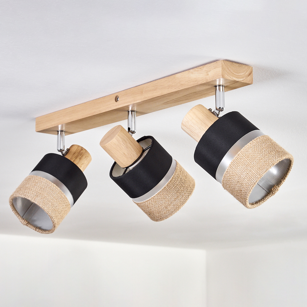 Eine Deckenleuchte mit drei Strahlern. Die Lampenschirme sind schwarz und beige mit Holz- und Metallakzenten.
