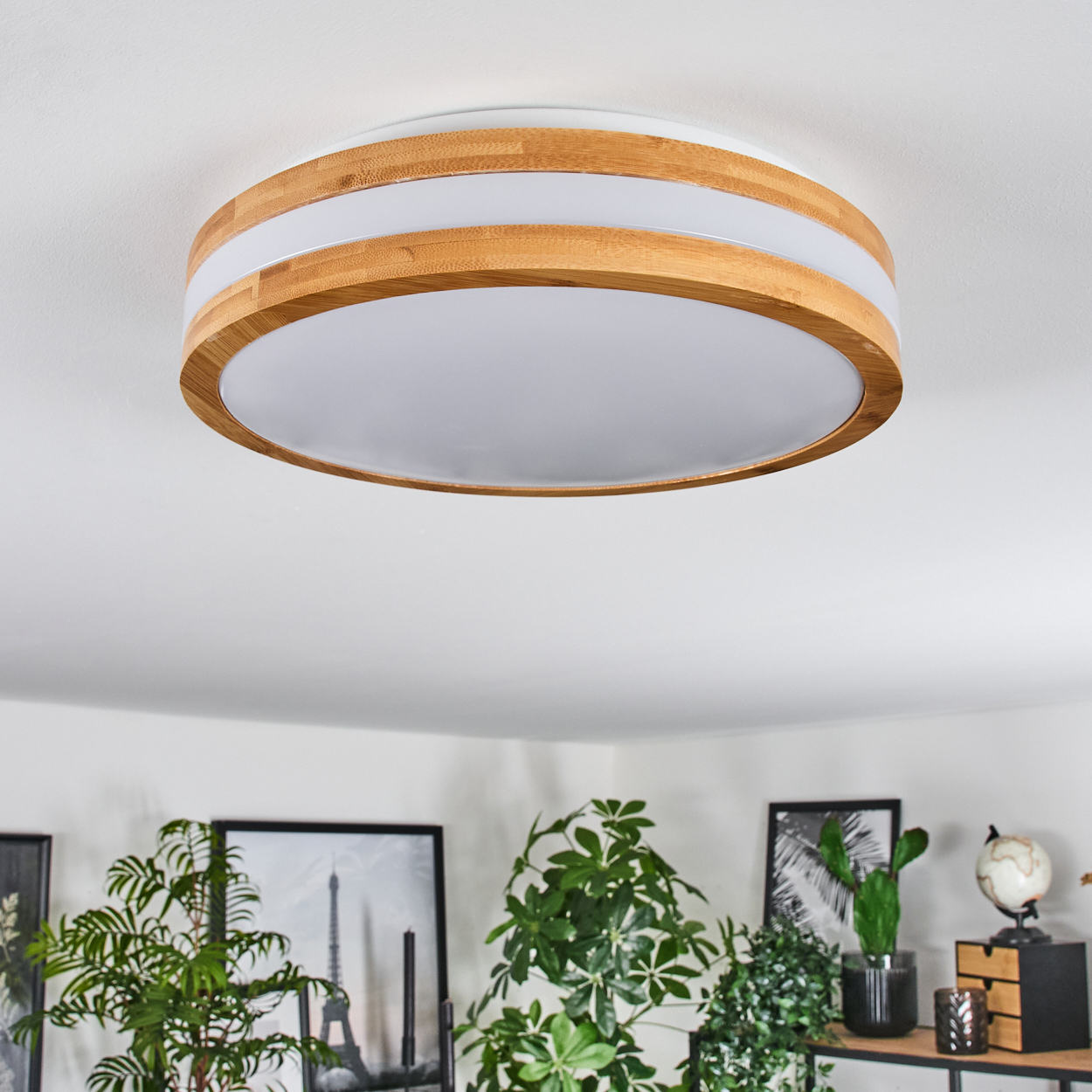 Eine moderne Deckenlampe aus Holz und weißem Licht. Pflanzen und Bilder sind darunter sichtbar.