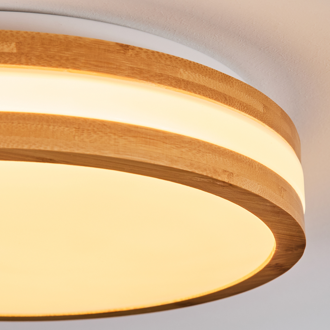 Eine runde Deckenleuchte. Sie hat einen Holzrahmen mit einem Lichtstreifen und einem leuchtenden, sanften gelben Licht.