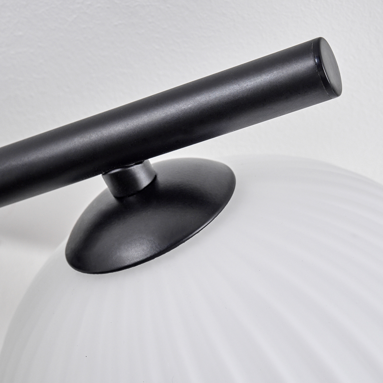 Nahaufnahme einer modernen Lampe. Sie hat einen schwarzen Arm und Sockel. Der Lampenschirm ist aus weißem, geripptem Glas.