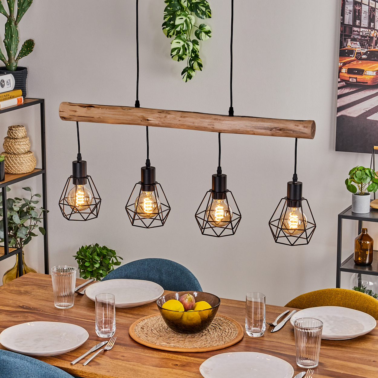 Esstisch mit Holzbalken-Leuchte. Teller, Gläser und eine Obstschale sind auf dem Tisch. Pflanzen im Hintergrund.