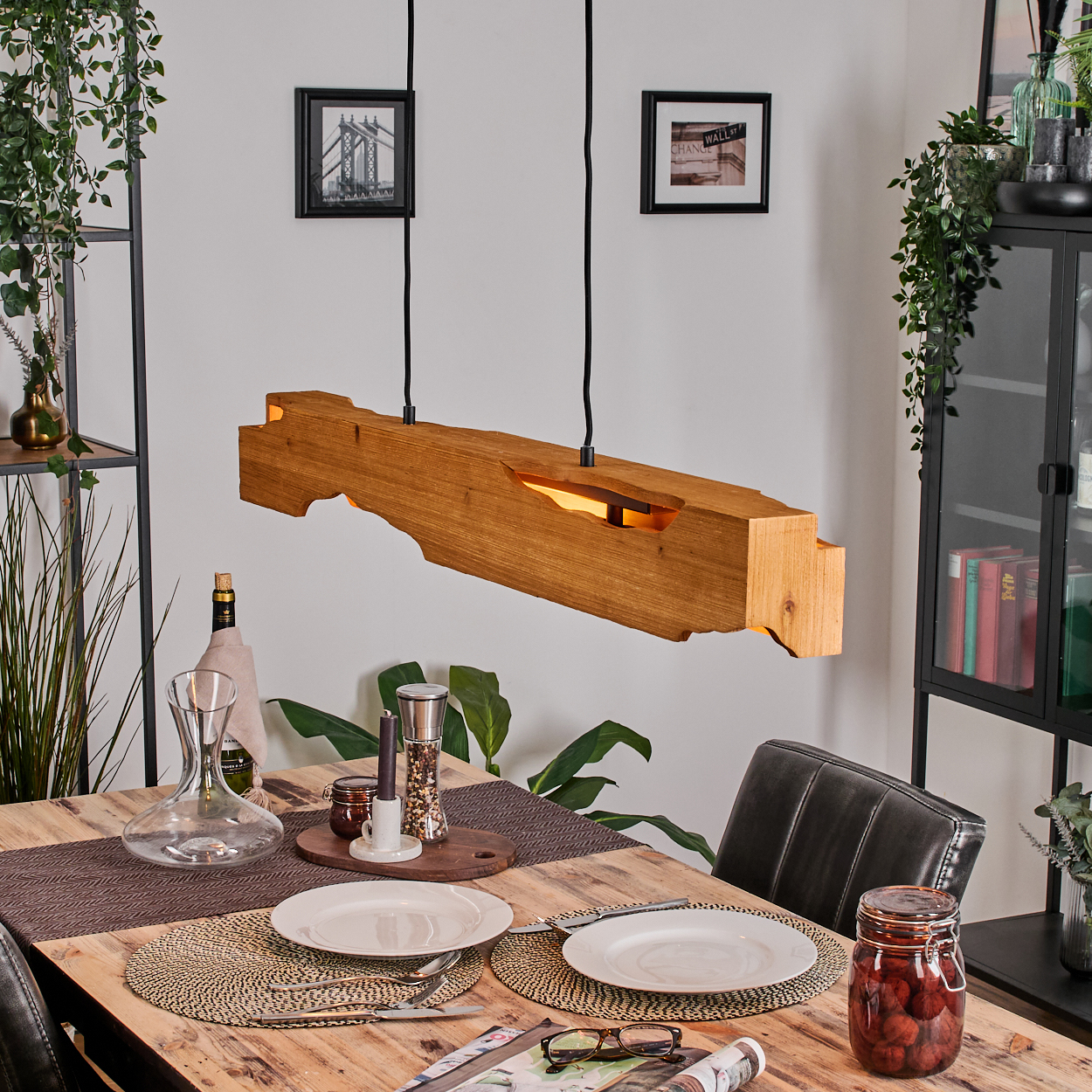 Holzbalkenleuchte über einem Tisch, der für eine Mahlzeit gedeckt ist. Teller, Gläser und ein Glas mit Essen sind zu sehen. Pflanzen und Rahmen sind im Hintergrund.