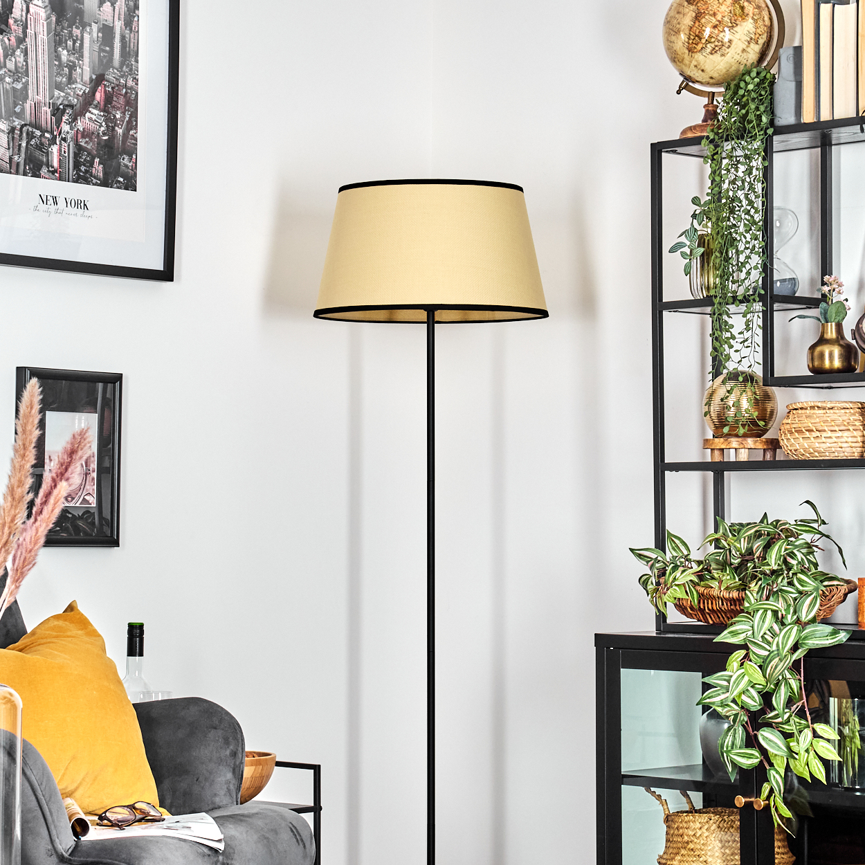 Ein Raum mit einer Stehlampe, einem schwarzen Metallregal mit Dekoration und einem grauen Sofa mit gelbem Kissen.