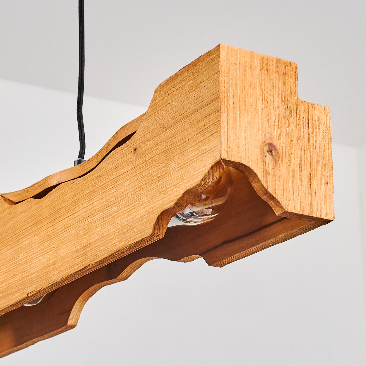 Eine Holzleuchte mit freiliegenden Glühbirnen hängt an einem schwarzen Kabel. Die Leuchte besteht aus hellbraunem Holz mit einem einzigartigen Schnitzmuster.