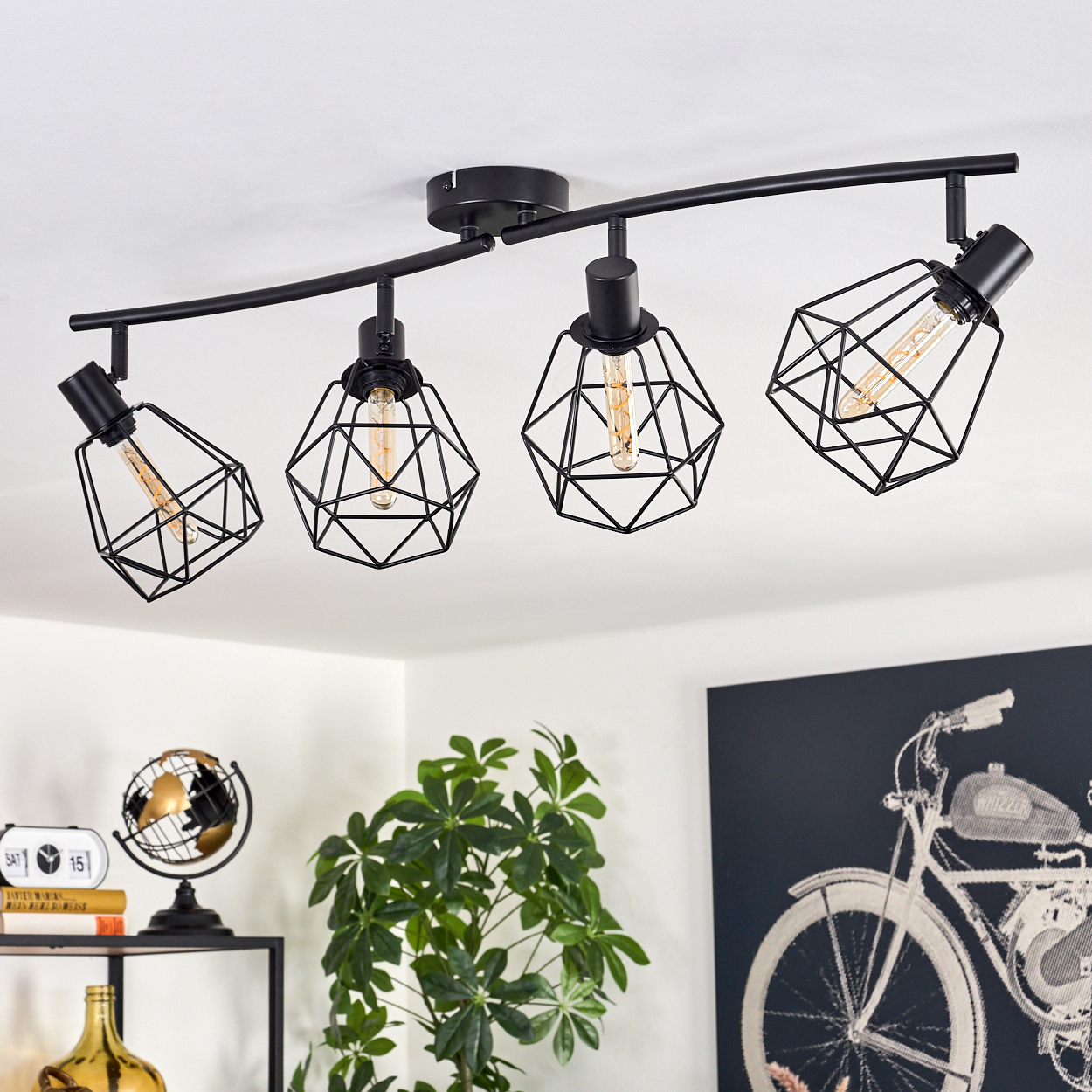 Schwarze Schienenbeleuchtung mit vier geometrischen Lampen. Im Hintergrund sind eine Pflanze, ein Globus und Fahrraderkunst zu sehen.