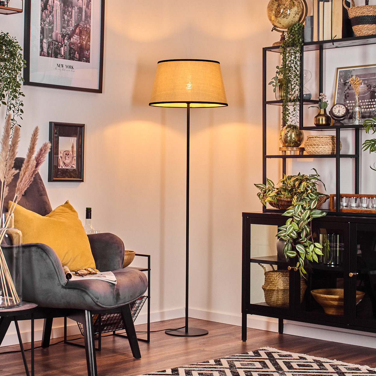 Gemütliches Wohnzimmer mit Stehlampe, Sessel und schwarzem Regal voller Deko. Ein Teppich und ein Bild an der Wand.