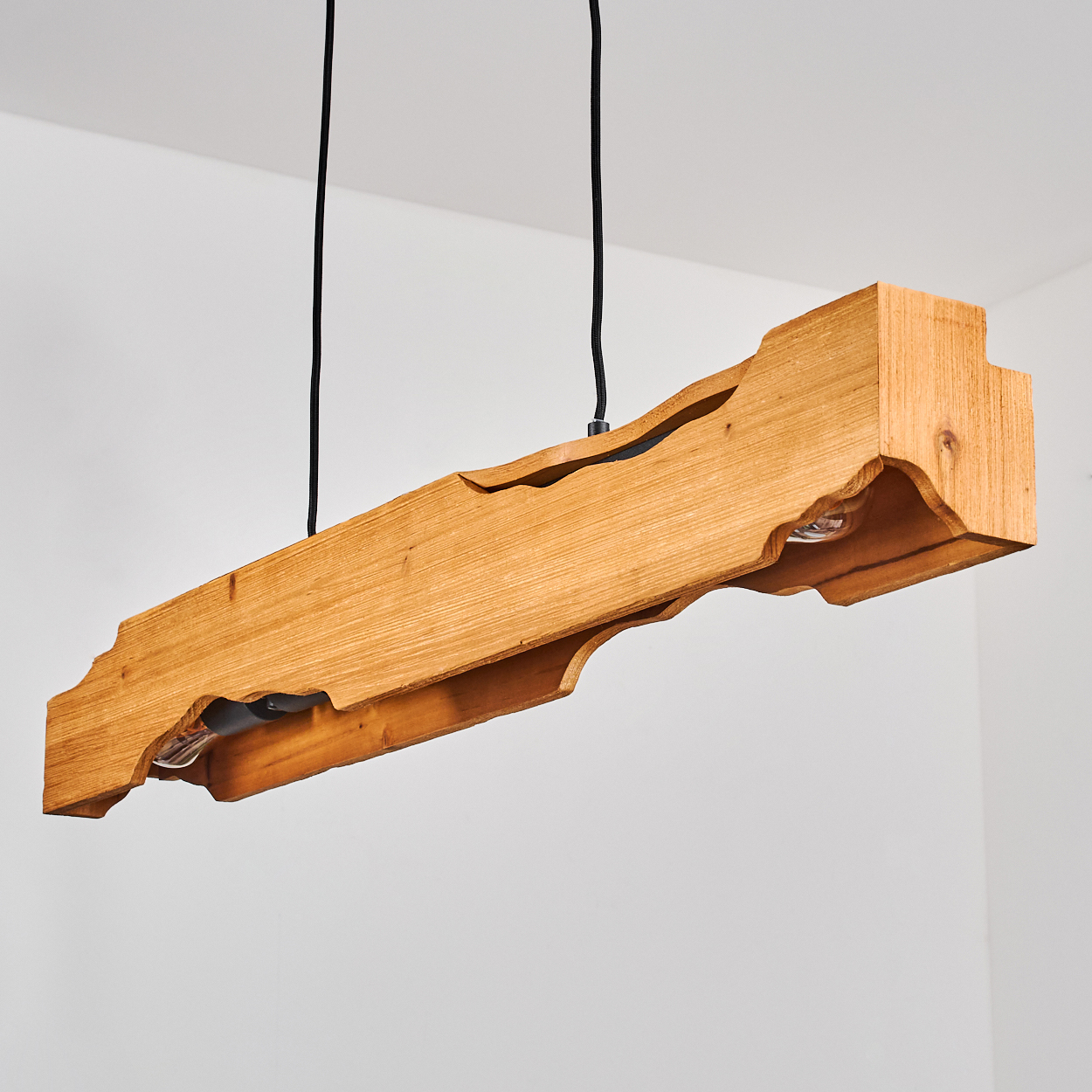 Eine rechteckige Holzlampe hängt an schwarzen Kabeln vor einer weißen Wand. Die Lampe hat zwei sichtbare Glühbirnen.