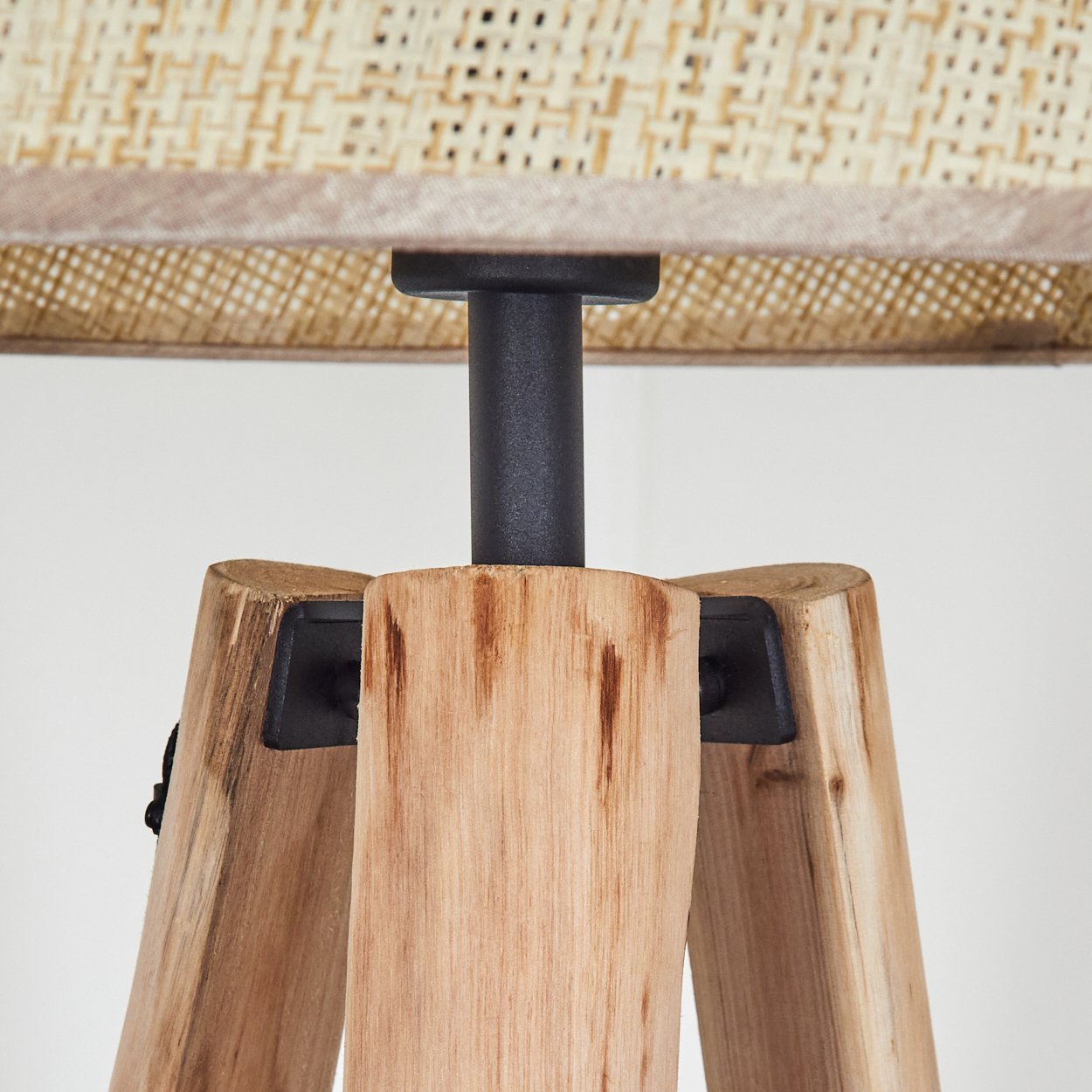 Eine Holzstativlampe mit gewebtem Schirm. Die Holzbeine tragen einen schwarzen Metallschaft, der Schirm ist beige.