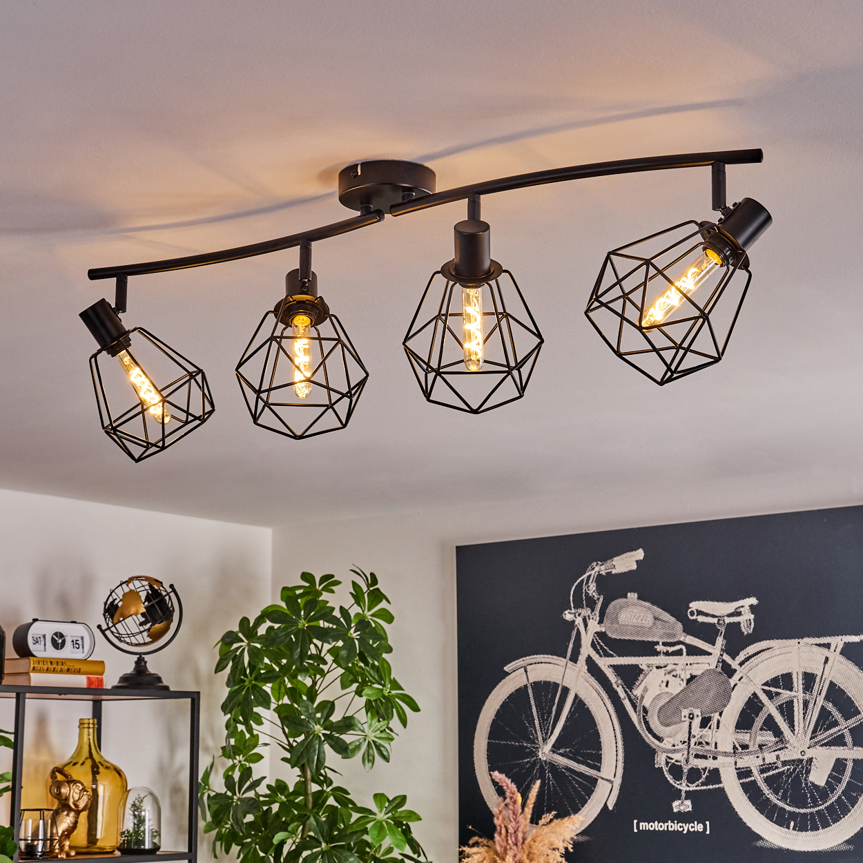 Deckenleuchte mit vier geometrischen Lampenschirmen. Darunter eine Pflanze, ein Globus und Motorradkunst.