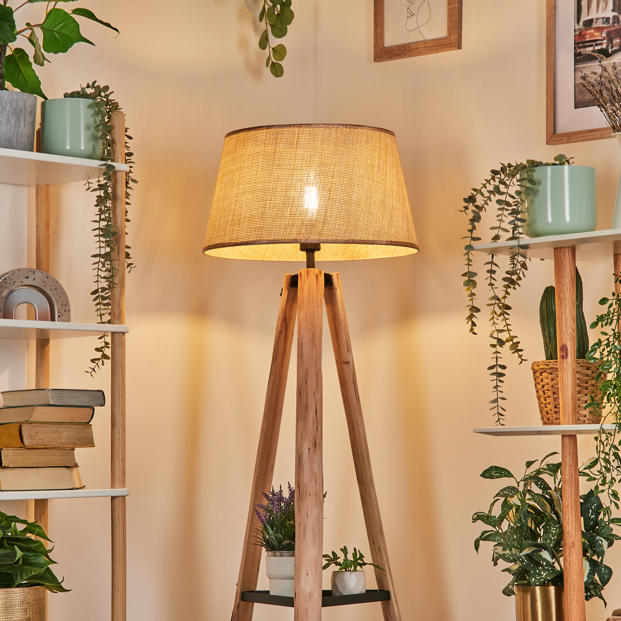 Eine hölzerne Stativlampe mit gewebtem Lampenschirm, umgeben von Bücherregalen, Topfpflanzen und gerahmten Kunstwerken.