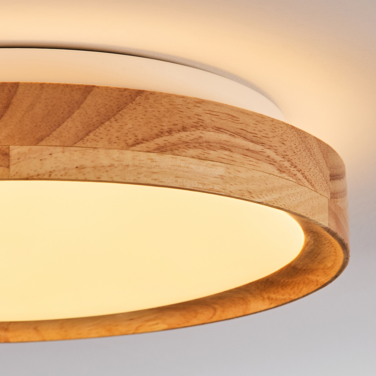Nahaufnahme einer modernen Deckenlampe. Sie hat einen Holzrahmen um ein Weiß und ein helles, gelbes Licht, das von der Mitte ausgeht.