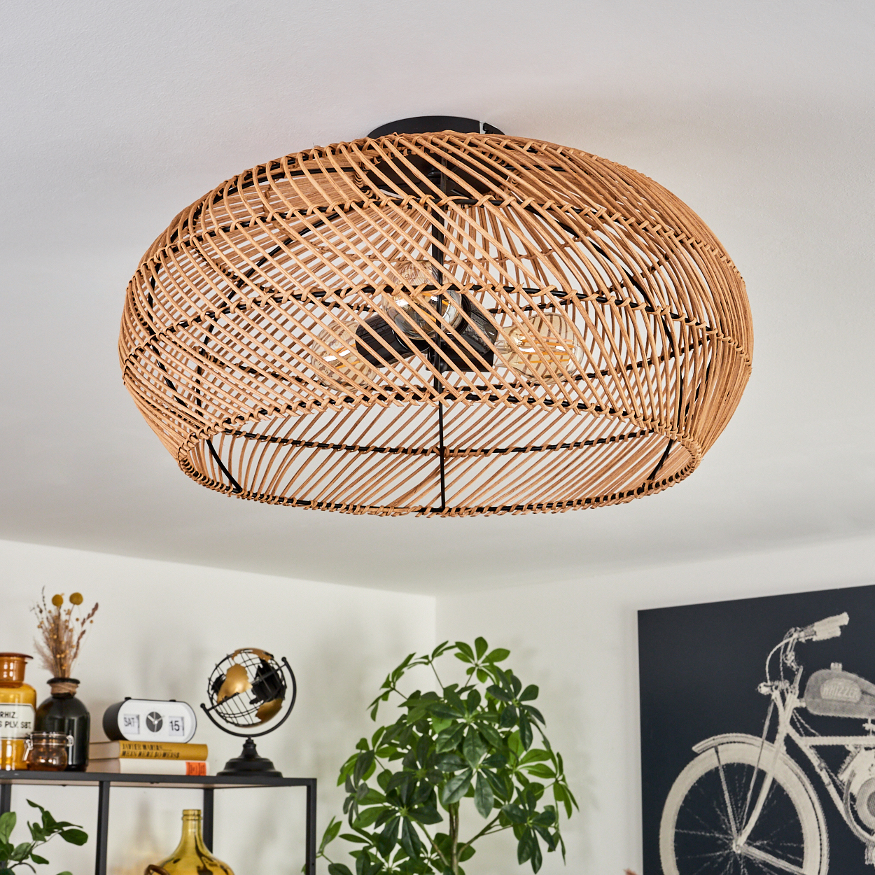 Eine gewebte Deckenlampe aus Rattan hängt über verschiedenen Dekorationsartikeln, darunter ein Globus, Pflanzen und ein Fahrradbild.