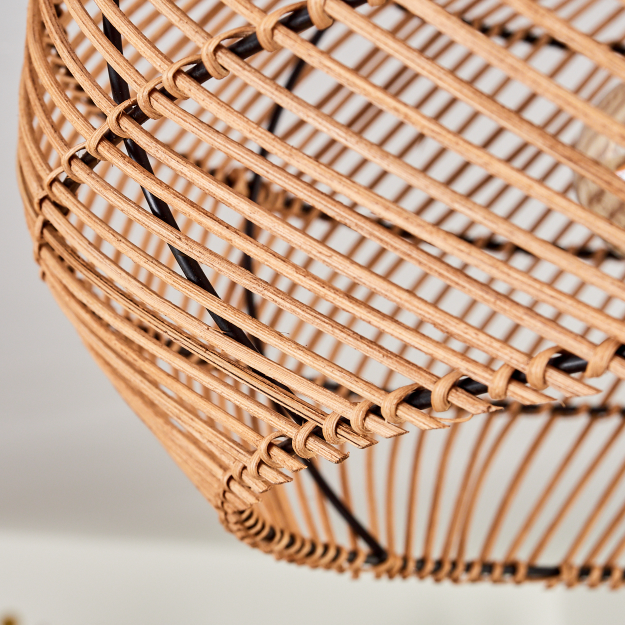 Nahaufnahme eines gewebten Lampenschirms aus Rattan. Der Schirm hat eine hellbraune Farbe, mit schwarzer Metallstützstruktur und weißem Hintergrund.
