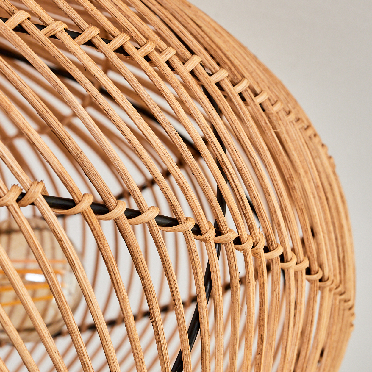 Nahaufnahme eines gewebten Lampenschirms aus Rattan mit schwarzem Metallrahmen. Der hellbraune Schirm hat eine kugelförmige Form.