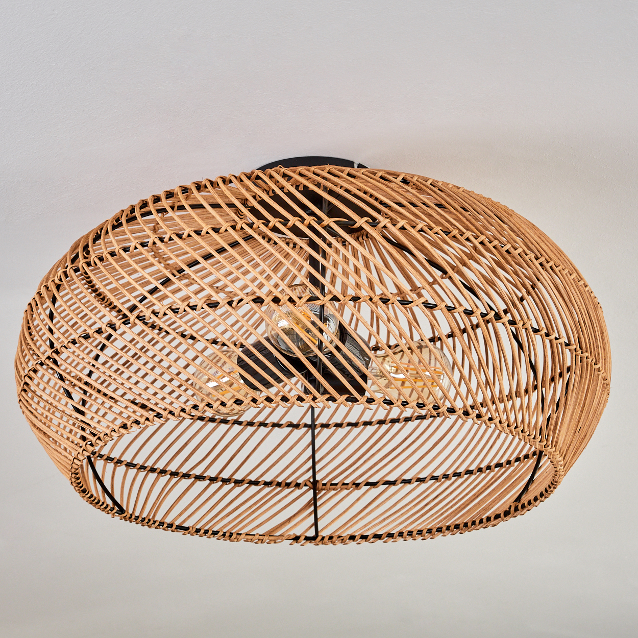 Eine gewebte Deckenleuchte aus Rattan mit zwei Glühbirnen. Die Leuchte ist vor einem weißen Hintergrund von der Decke abgehängt.