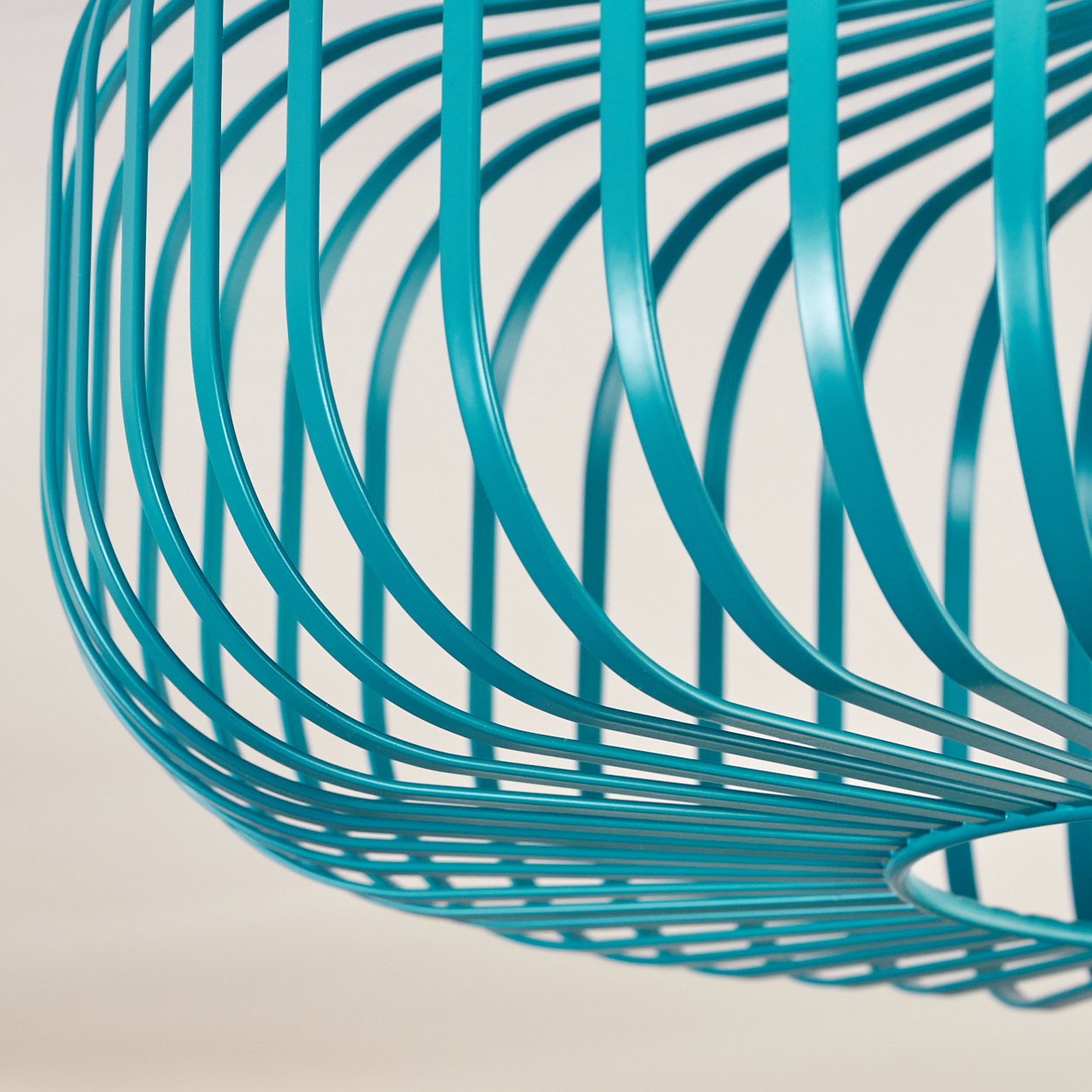 Nahaufnahme einer teal-farbenen Metallstruktur mit gebogenen Stäben, die eine käfigartige Form bilden, vor hellem Hintergrund.