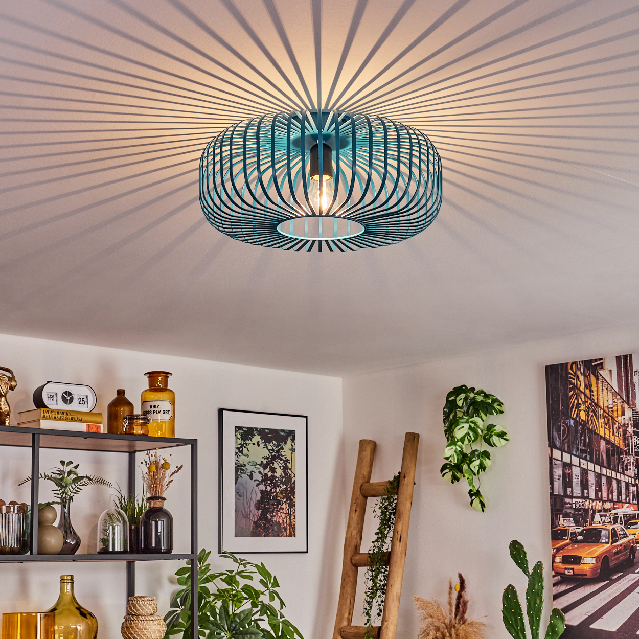 Eine türkisfarbene Deckenlampe wirft Streifenschatten. Darunter Regale mit Deko und Pflanzen. Eine Holzleiter und ein Bild an der Wand.